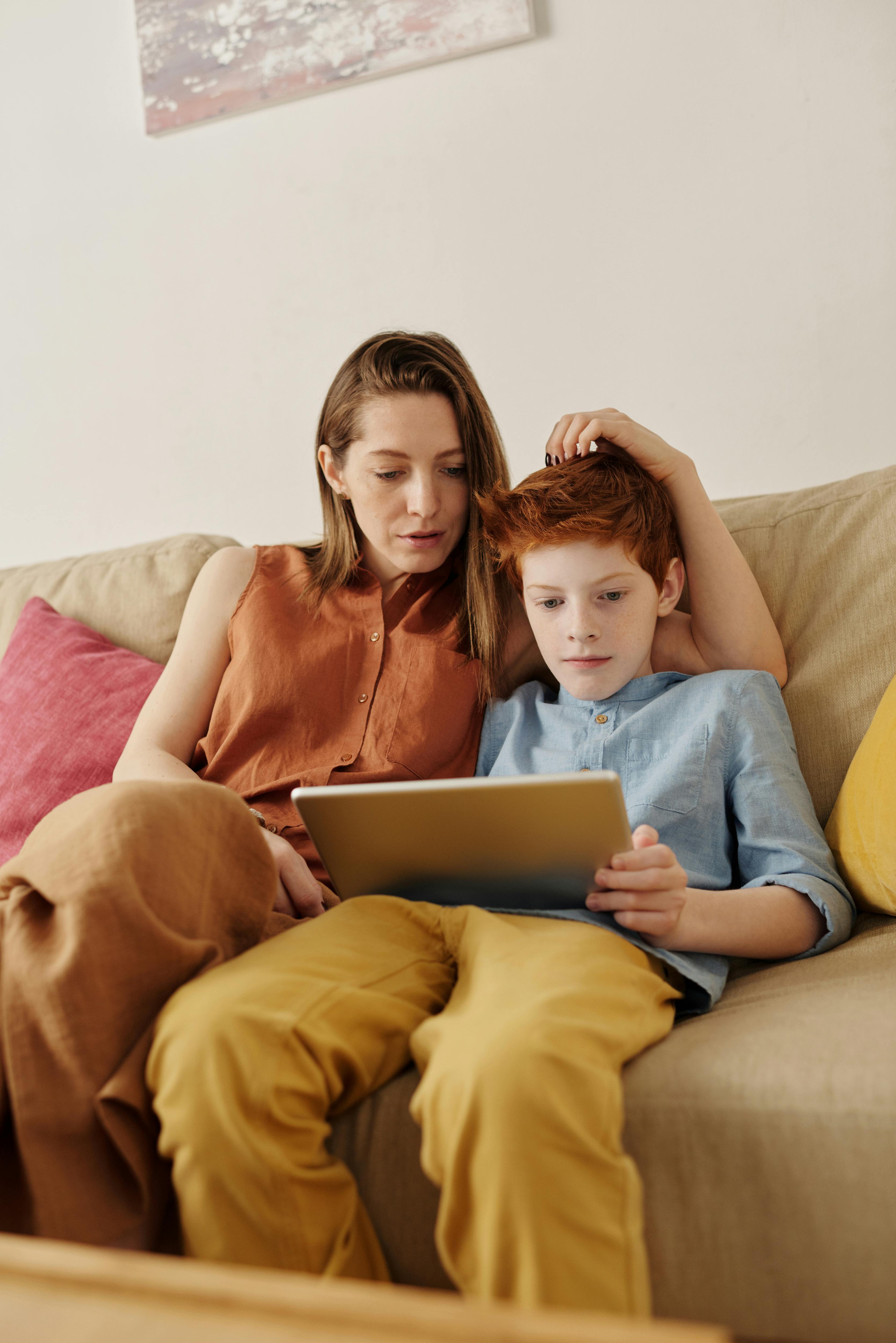 A mother and her son sitting on a couch, using a tablet for education and bonding time.