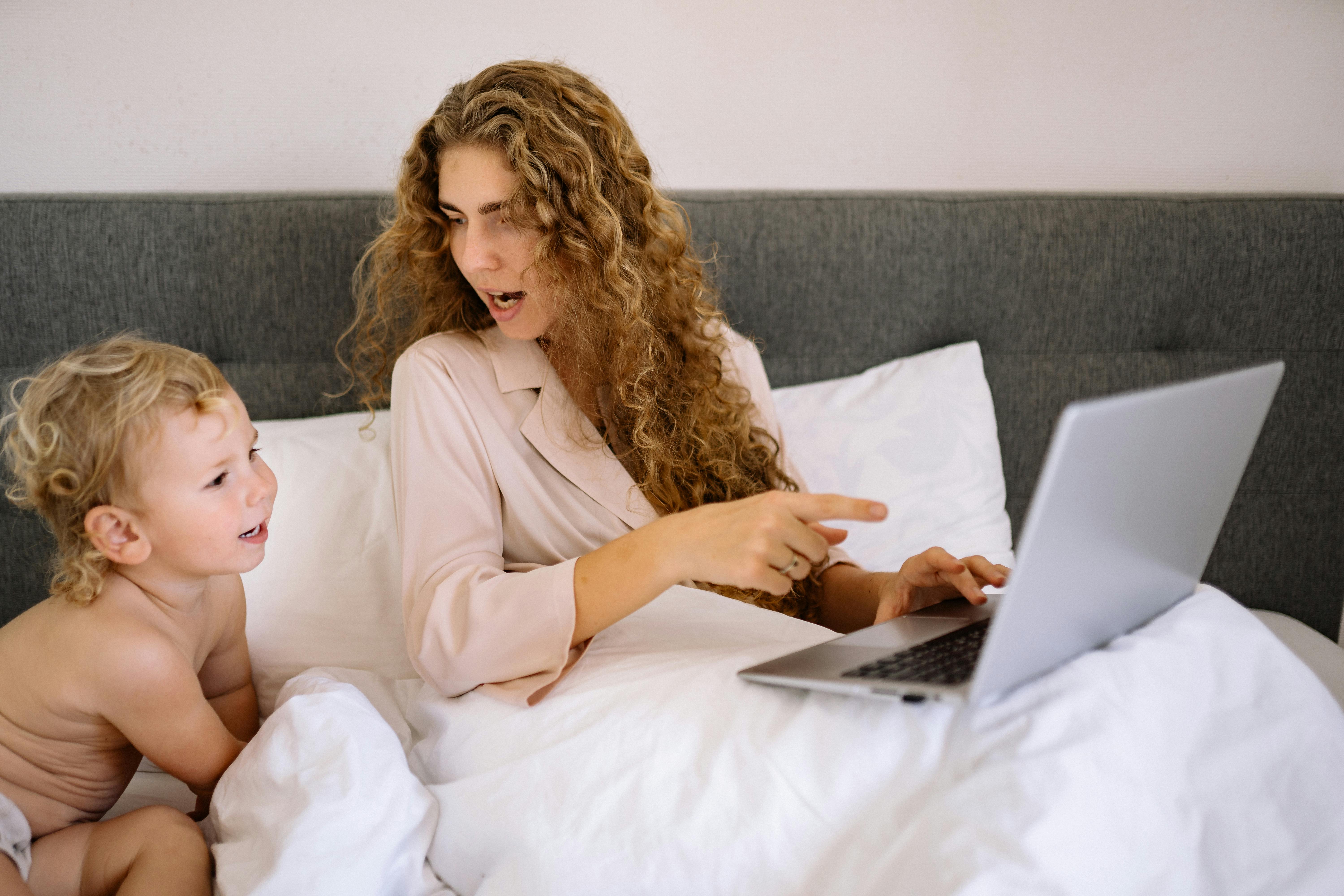 A mother and her toddler sharing a moment in bed with a laptop, illustrating work-life balance.